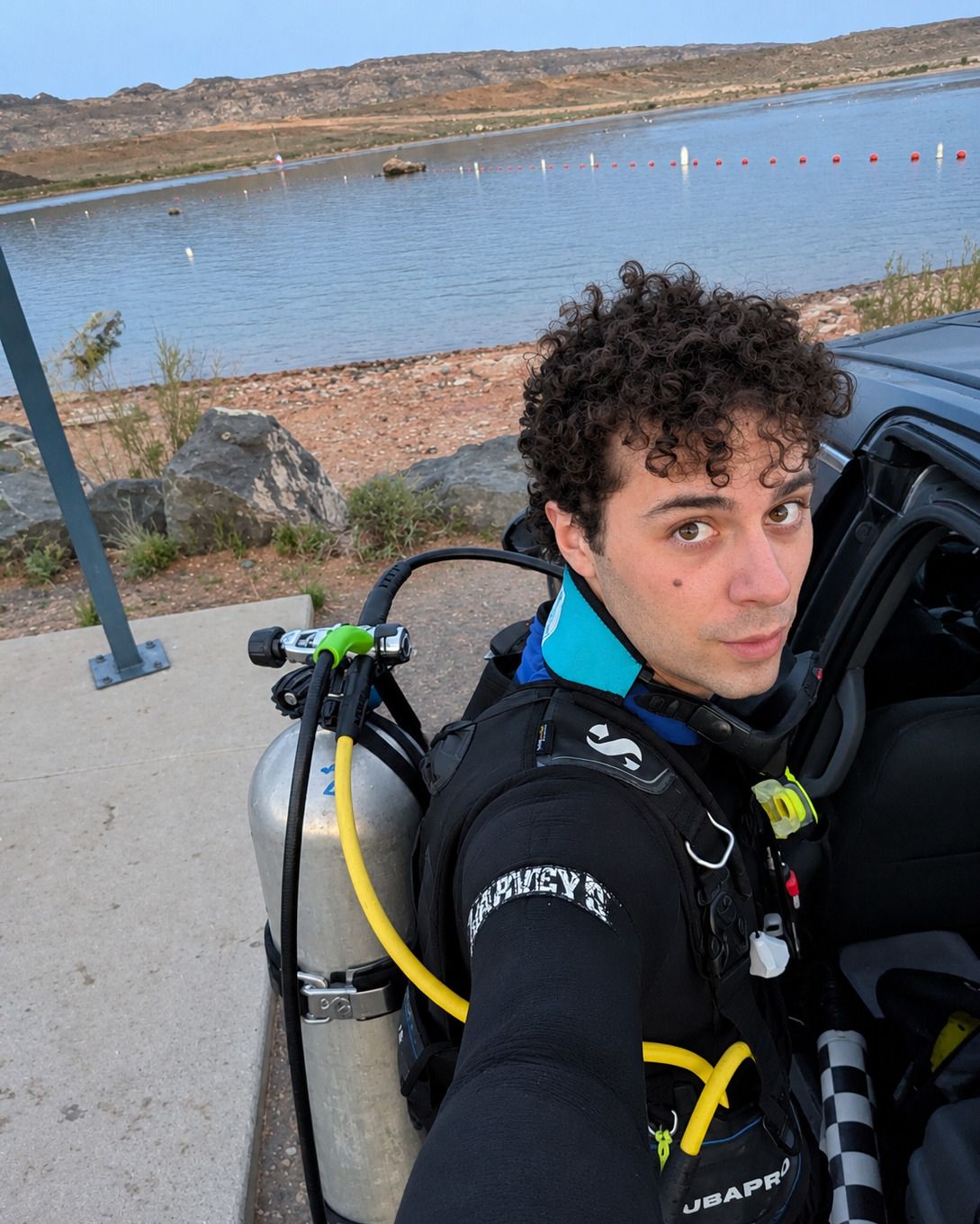 Jacob in a wetsuit and scuba gear at the edge of a lake, before a dive